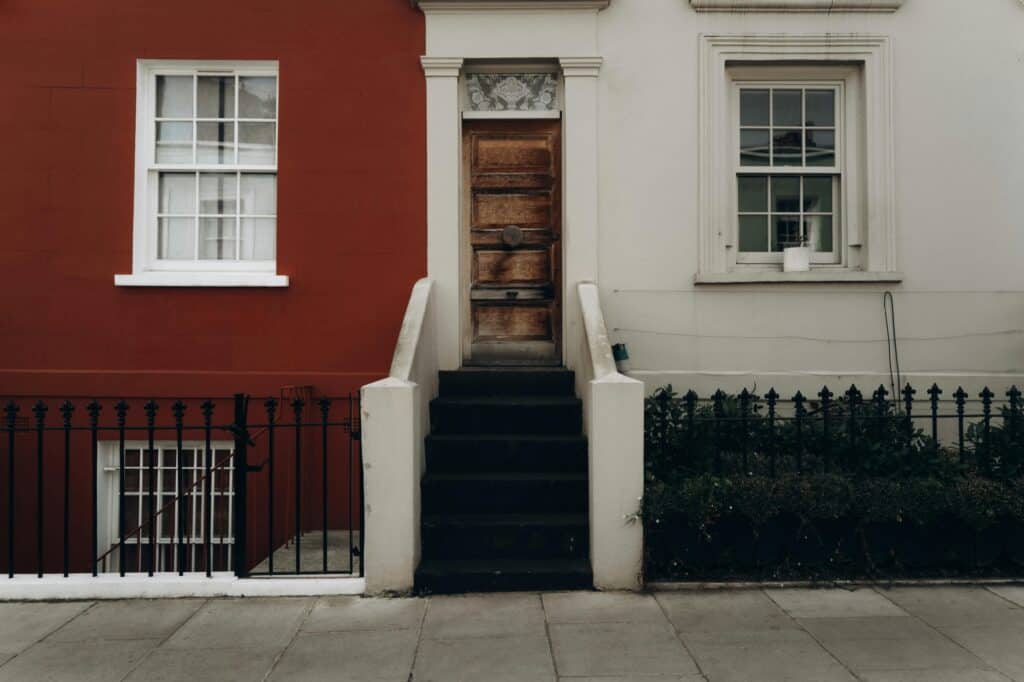 In front of simple British townhouse with staircases and railings in the concept of 'best affordable housing options in North London'.