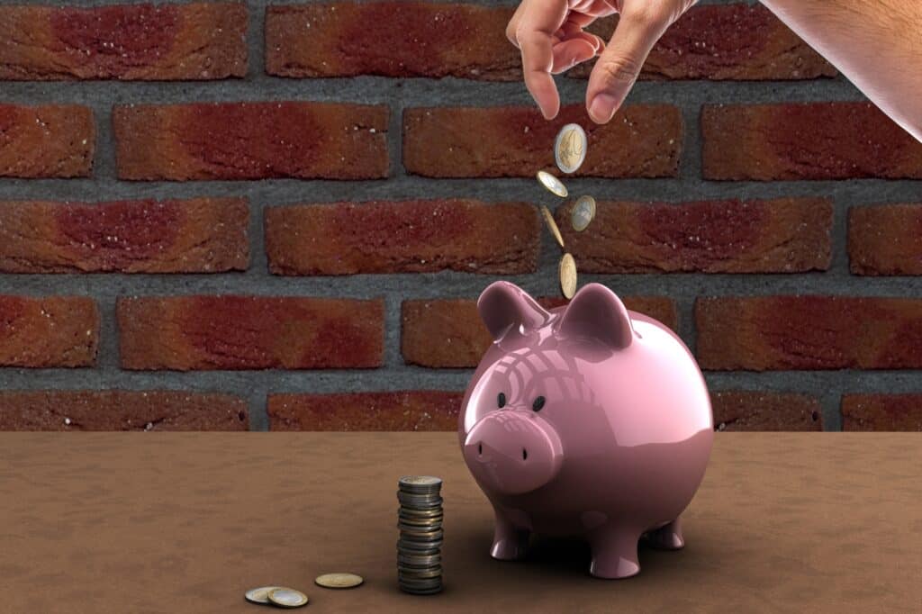 A glossy piggy bank with coins falling into it in the concept of 'how to save money when moving to North London'.