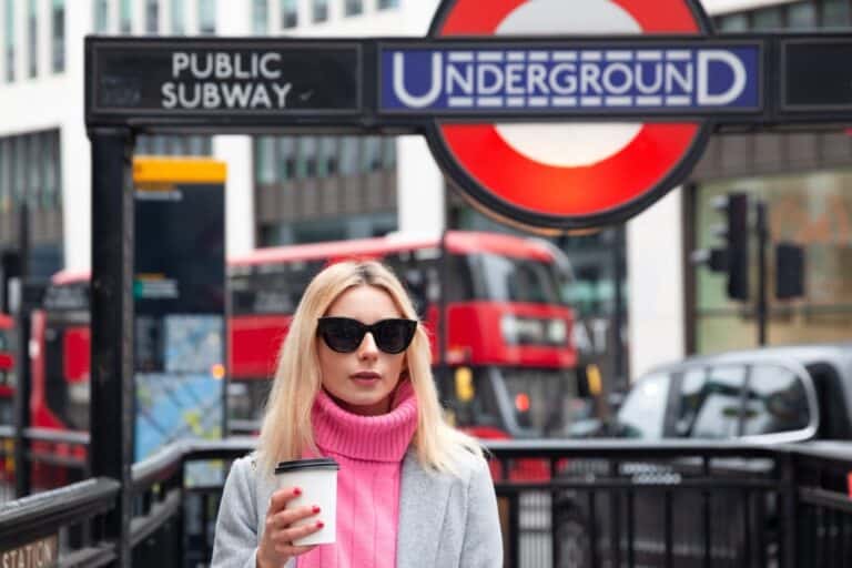 Public subway sign and double decker buses in the background of a woman in the concept of 'how to use North London's public transport'.
